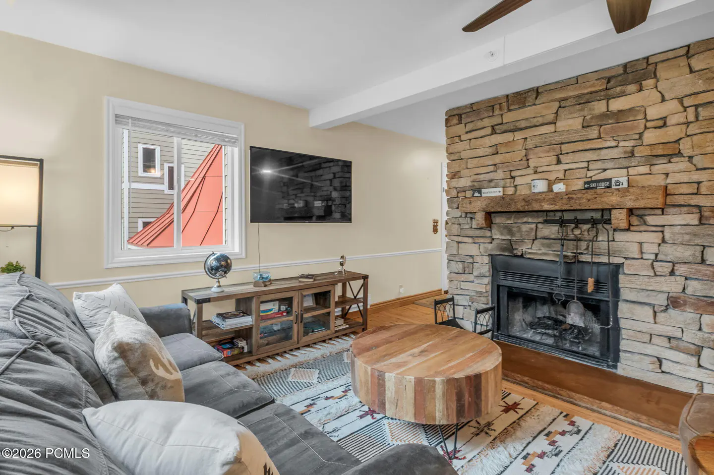 Living room with a gray sofa, stone fireplace, wood coffee table, and a TV above a wooden console table.