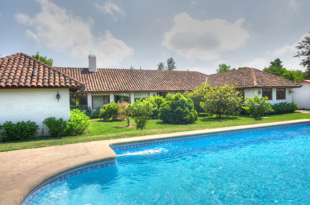 Backyard view of a white house with a red tile roof and a blue swimming pool.