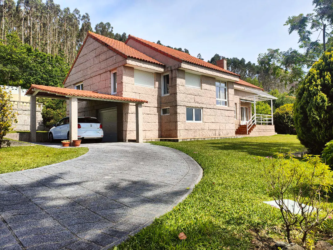 Exterior view of a two-story stone house with a red tile roof, a driveway, and a white car parked in a carport.