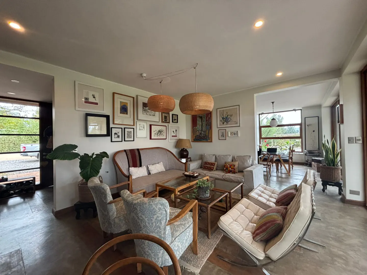 A living room with sofas, chairs, and artwork on the walls. Two rattan pendant lights hang from the ceiling.