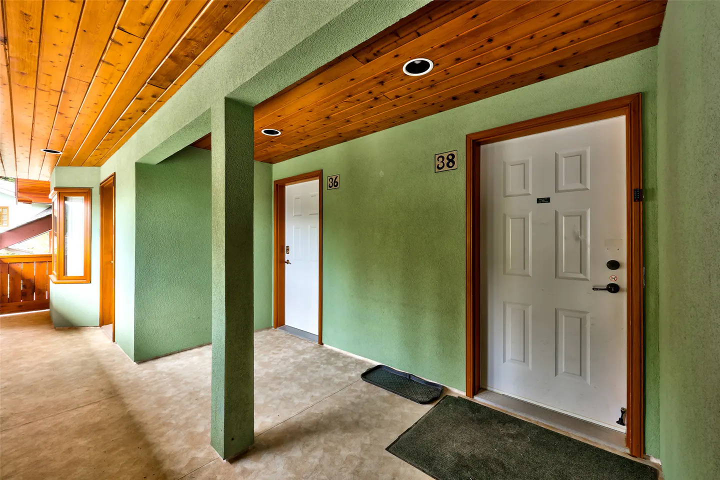 Hallway with green walls and a wood ceiling. White doors with brown trim are numbered 36 and 38. A dark mat sits in front of each door.