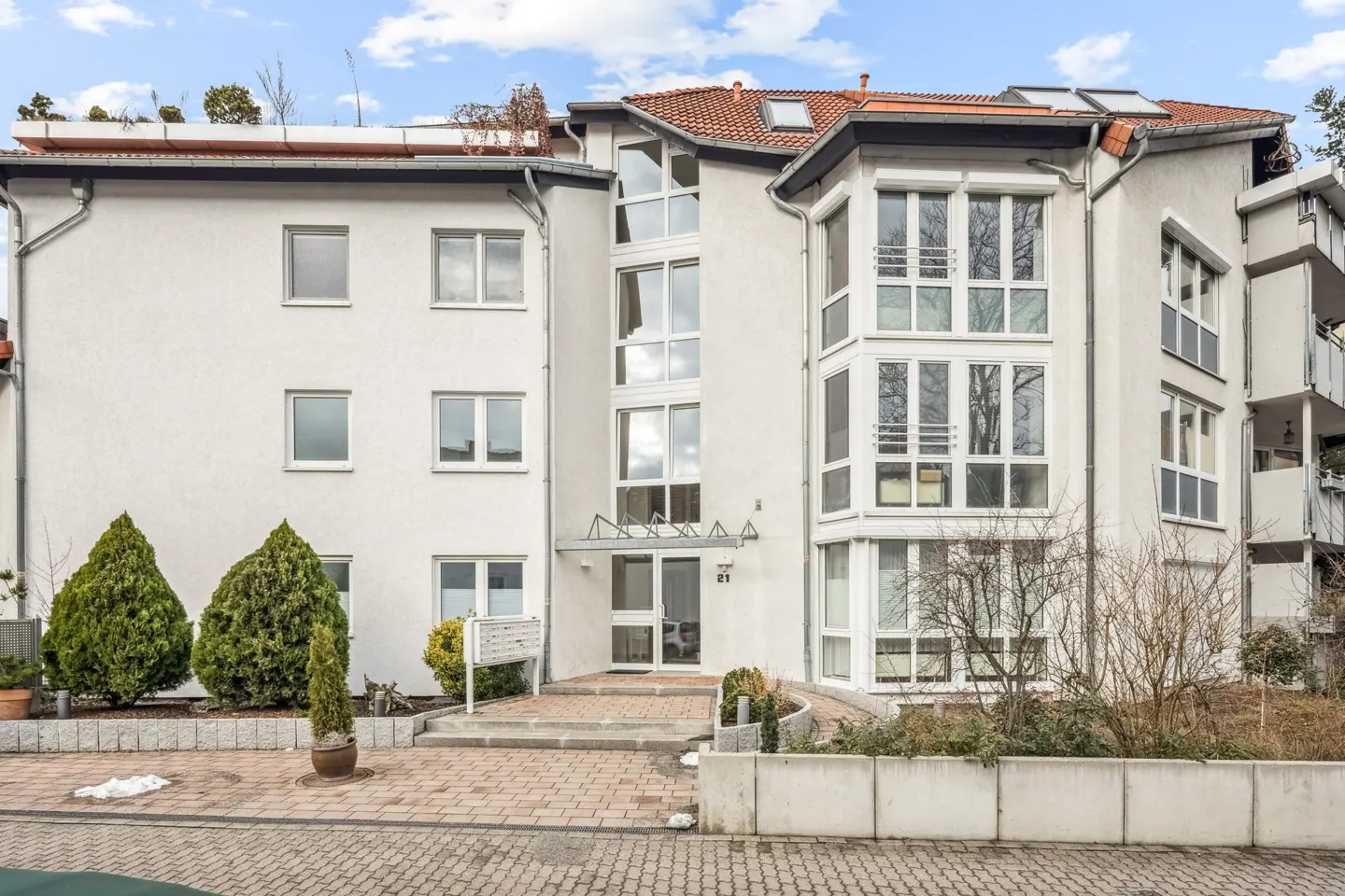 Exterior of a three-story white apartment building with many windows and a red tile roof.