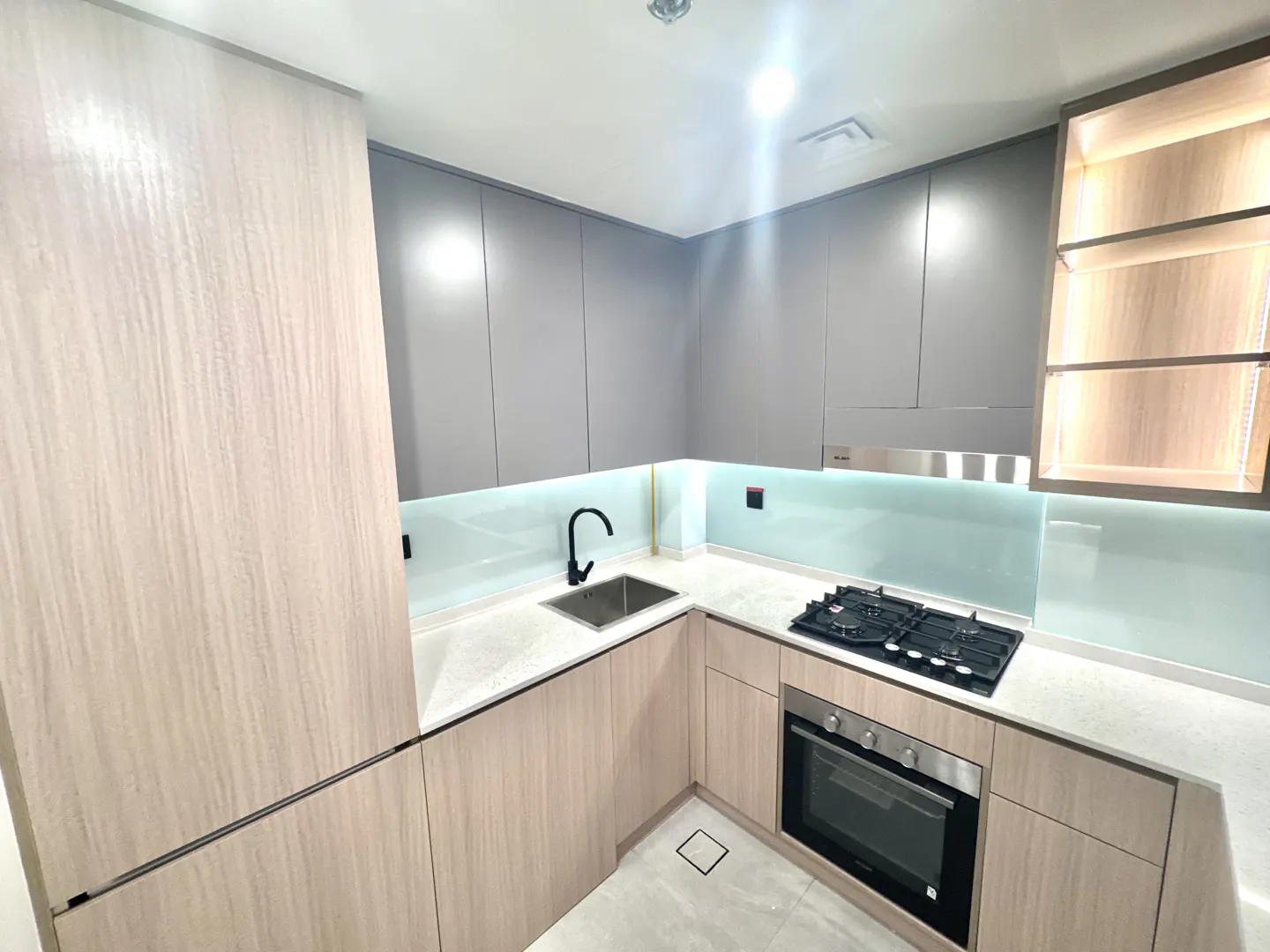 Modern kitchen with gray upper cabinets, light wood lower cabinets, stainless steel oven, and black gas stovetop.