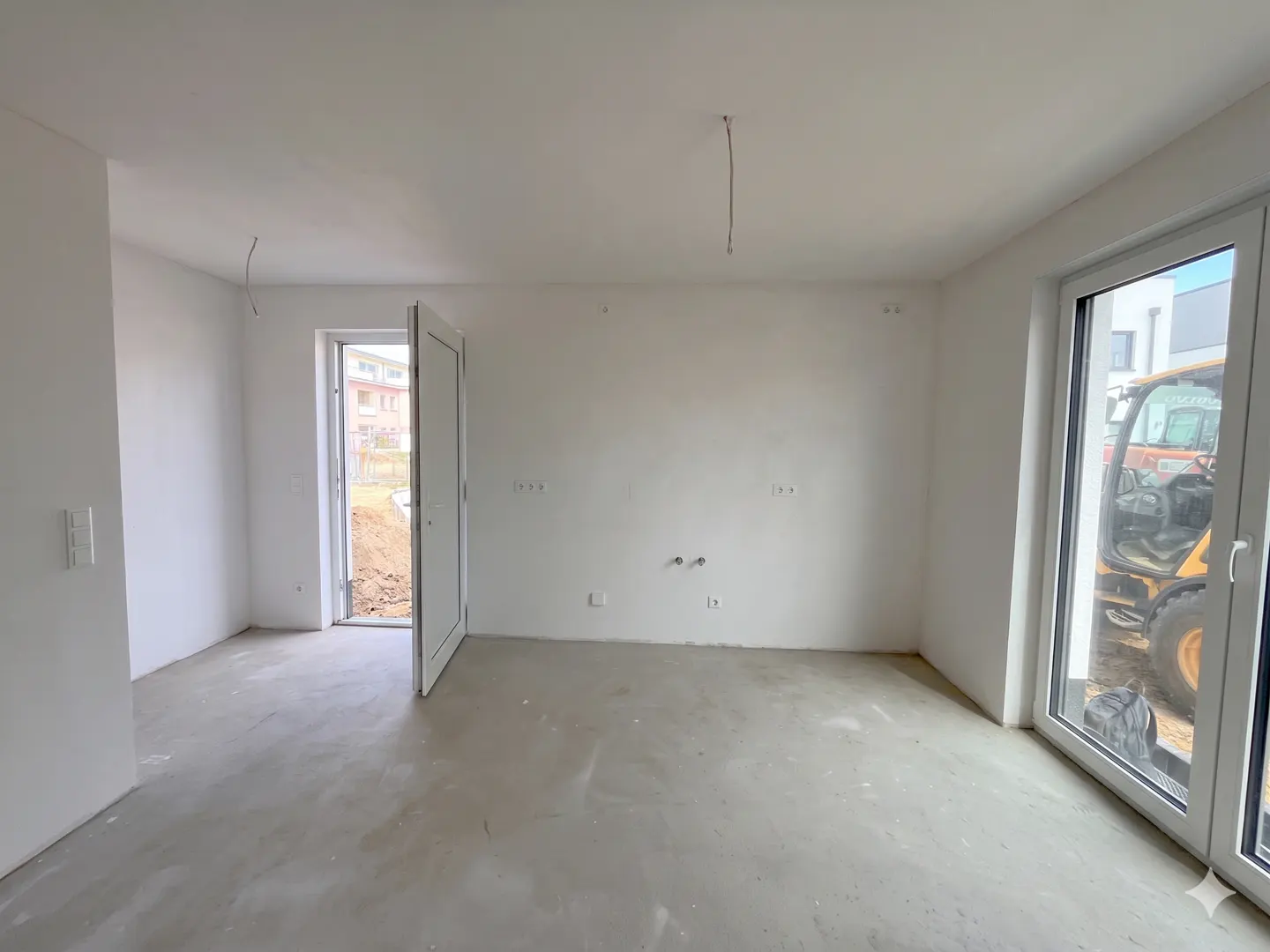 Unfinished room with white walls, a gray concrete floor, and an open white door. Outside the window is a yellow construction vehicle.