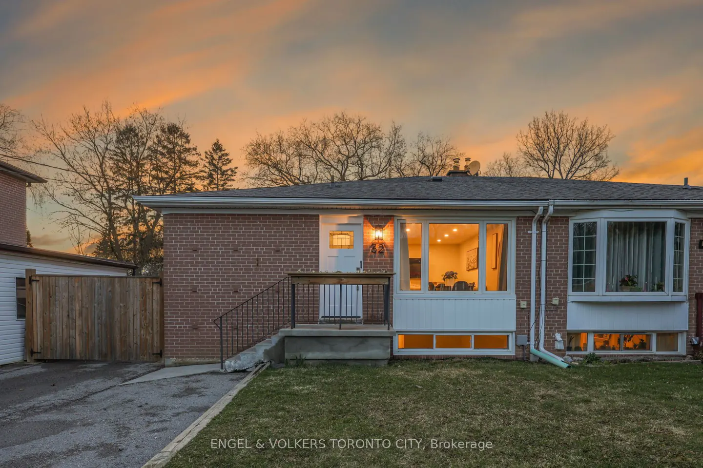 Exterior view of a red brick house with a small front lawn at sunset. The house has a white door and large windows.