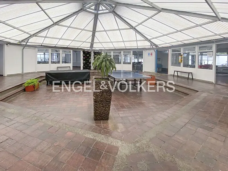 Indoor courtyard with brick floors, a ping pong table, and a white metal roof. The Engel & Volkers logo is superimposed on the image.