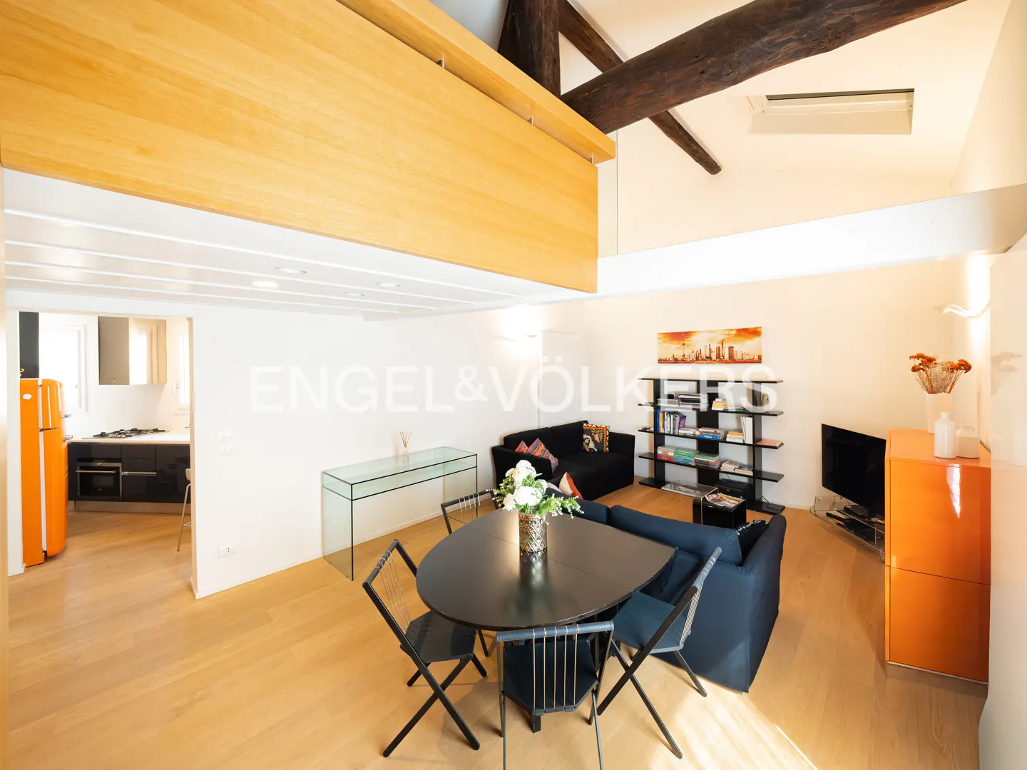 Bright, modern apartment interior with wood floors, black dining set, blue sofa, and orange fridge. Exposed beams add character.