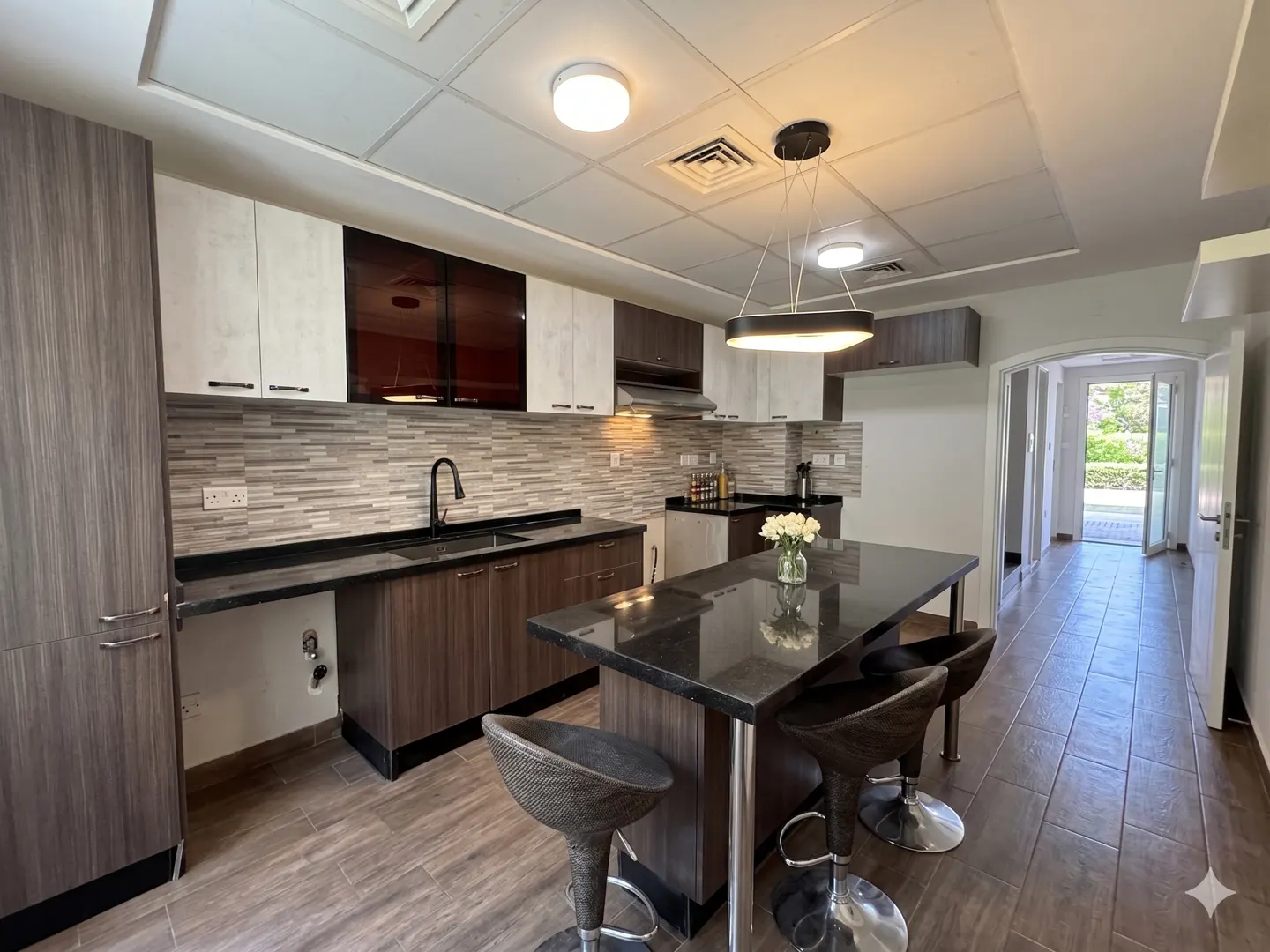A modern kitchen with brown cabinets, a black countertop, and a center island with three stools.