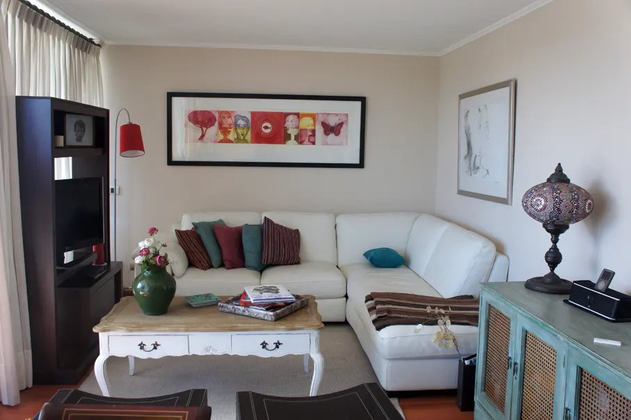 Living room with a white sectional sofa, a coffee table with flowers, and colorful artwork on the wall.