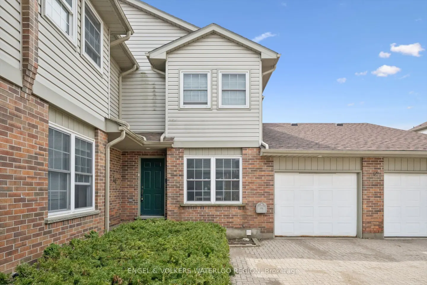 Exterior of a two-story townhouse with brick and siding, a green door, and a white garage door.