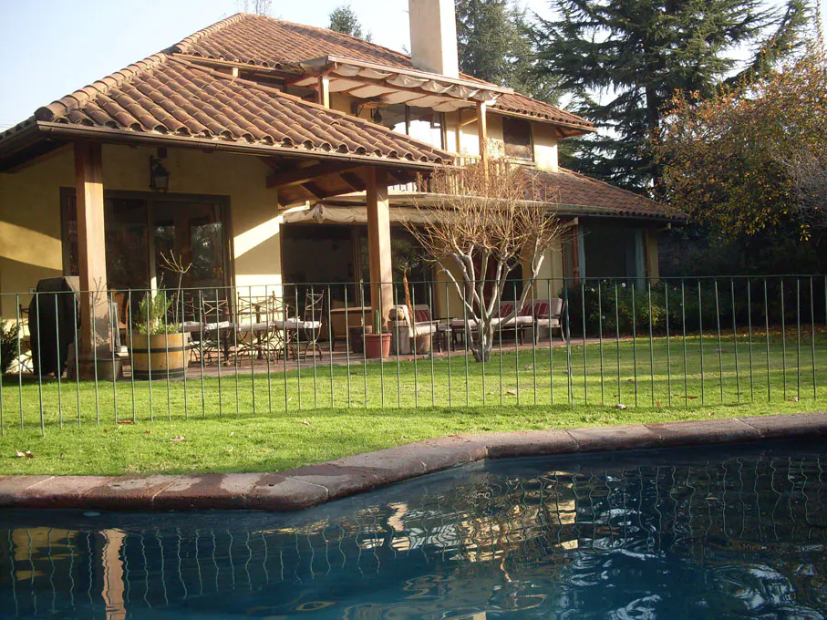Exterior view of a tan house with a red tile roof, a pool, and a green lawn.