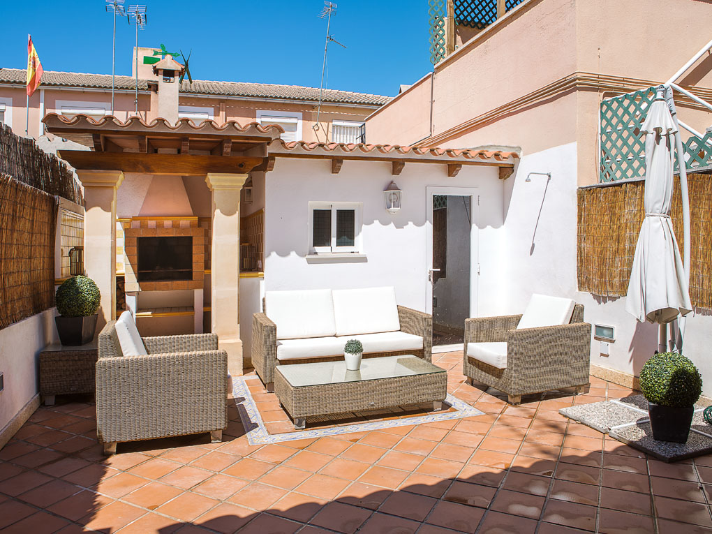 Sunny patio with wicker furniture, a glass coffee table, and a built-in outdoor fireplace on a terracotta tiled floor.