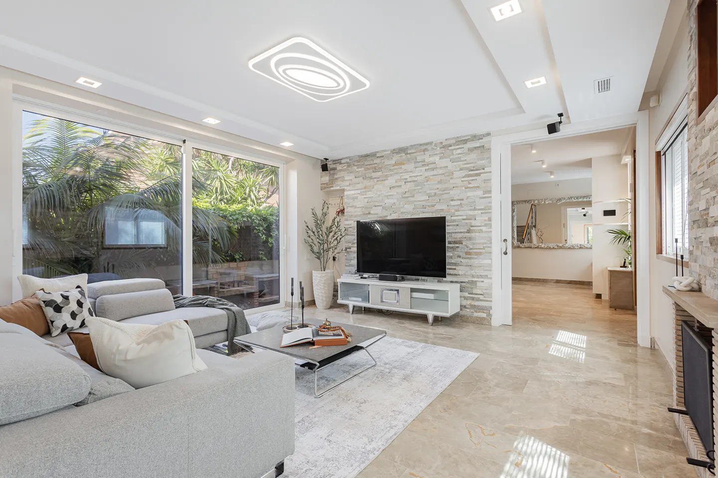 Bright living room with gray sofa, stone accent wall, and large sliding glass doors to a lush green yard.