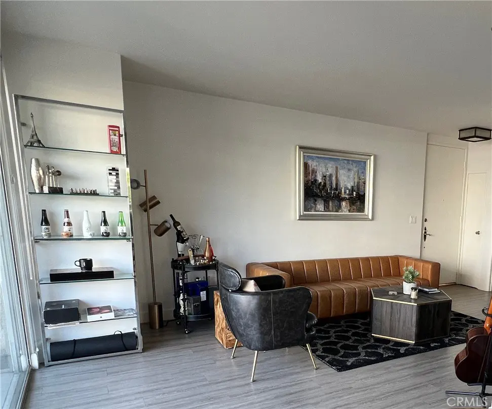 Living room with a brown leather sofa, black chair, and a glass shelving unit. A cityscape painting hangs on the wall.