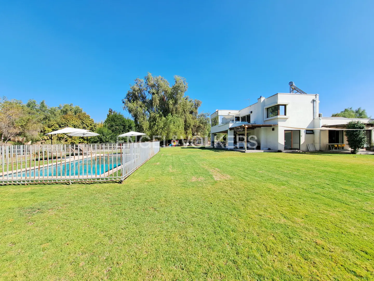 Exterior view of a modern white house with a pool, green lawn, trees, and blue sky.
