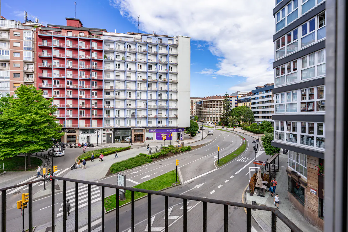 View from a balcony overlooking a city street with colorful buildings, pedestrian walkways, and a bus stop.