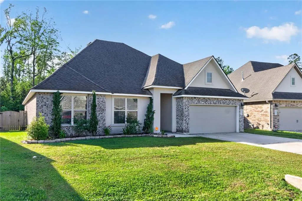 A single-story home with a gray roof, stone accents, and a green lawn under a blue sky.
