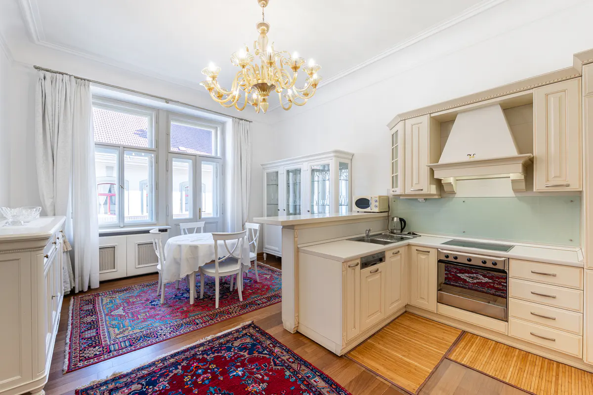 Bright, open kitchen with white cabinets, a dining table with white chairs, and a red patterned rug. A gold chandelier hangs from the ceiling.