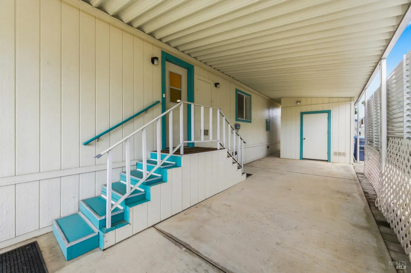 Exterior view of a white house with turquoise trim, stairs, and a covered patio. White railings lead to the front door.