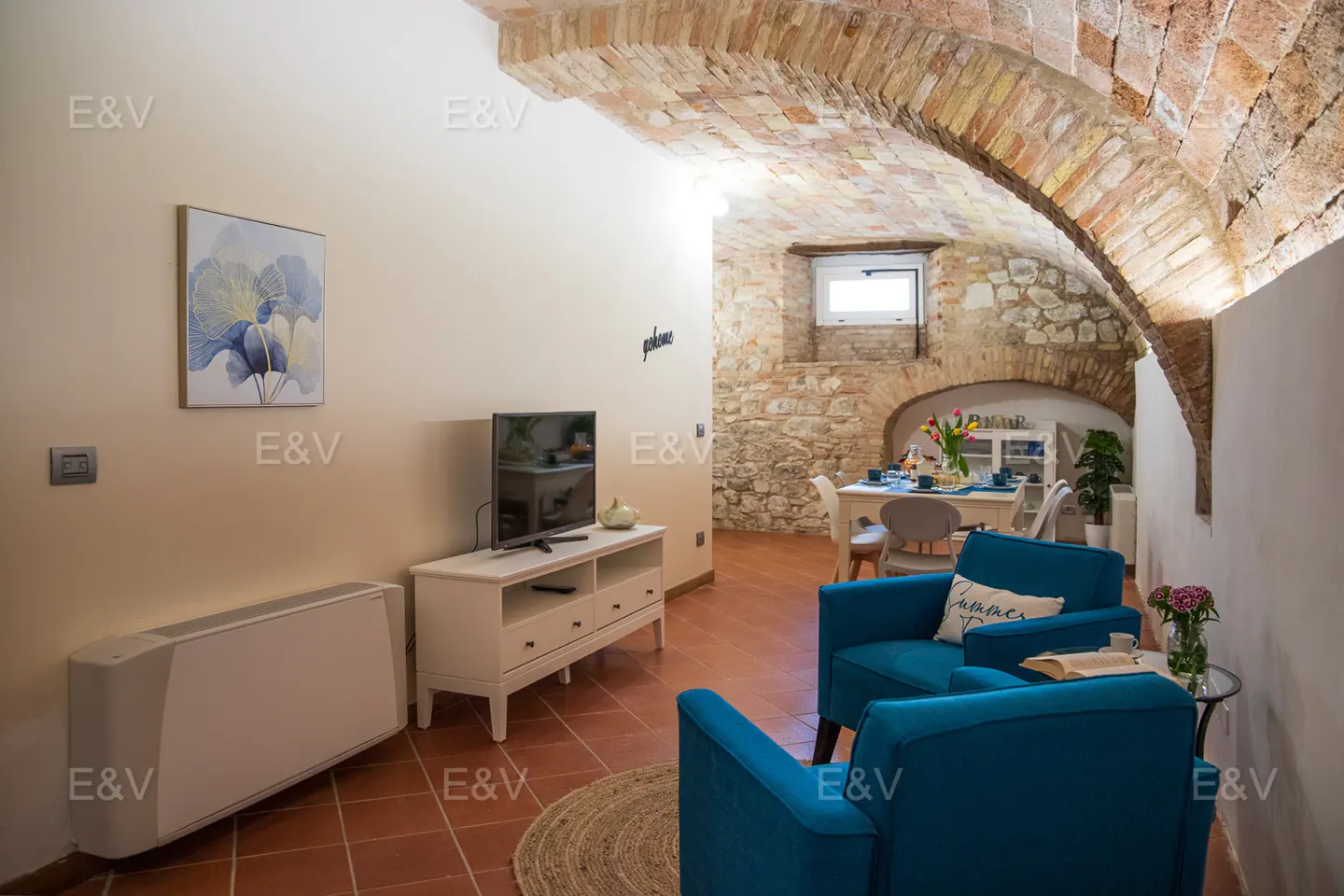 Living room with brick archway, blue chairs, TV, and dining area in the background.