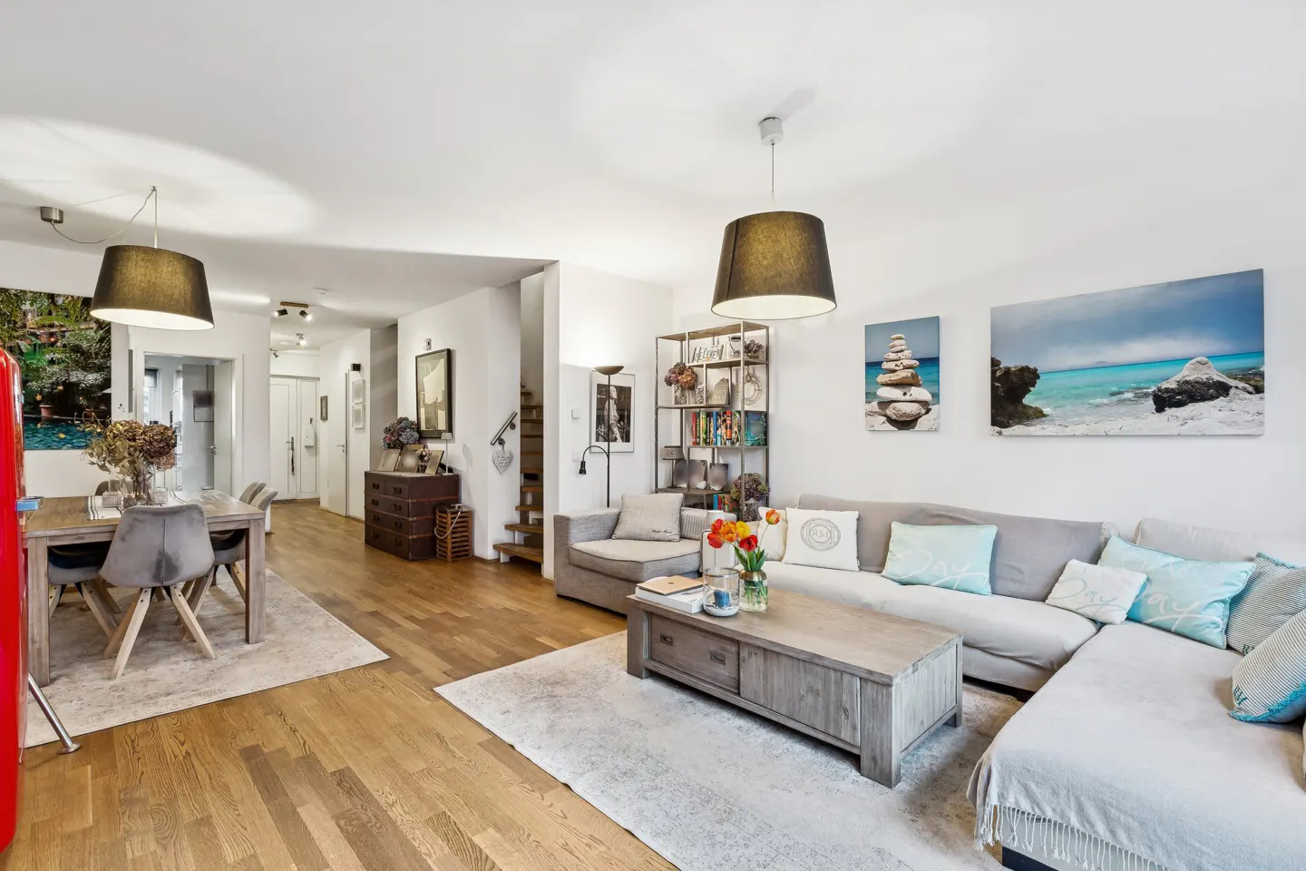 Bright living room with hardwood floors, a gray sectional sofa, a wooden coffee table, and a dining table with gray chairs.