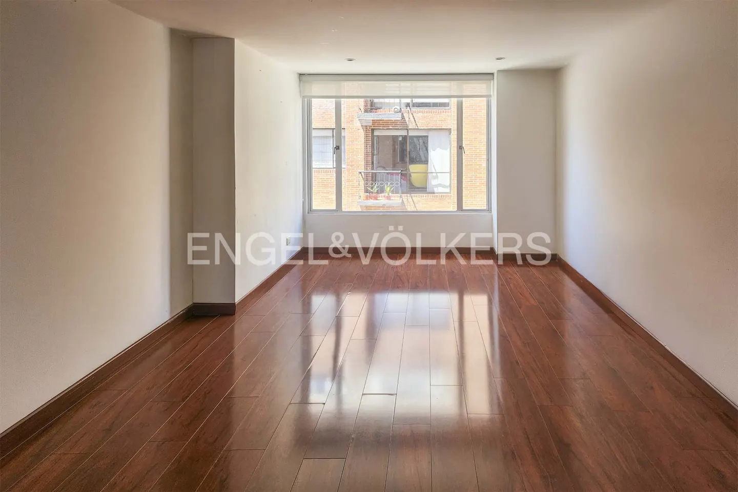 Empty room with hardwood floors, white walls, and a large window showing a brick building.