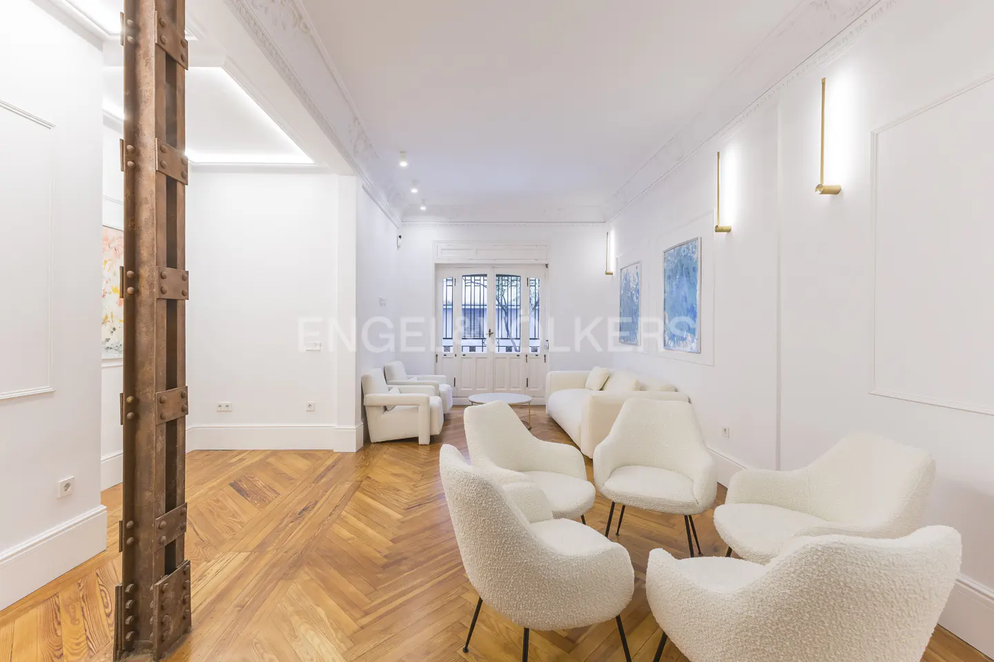Bright living room with white walls, herringbone wood floors, and white furniture. A rustic metal beam stands near the wall.