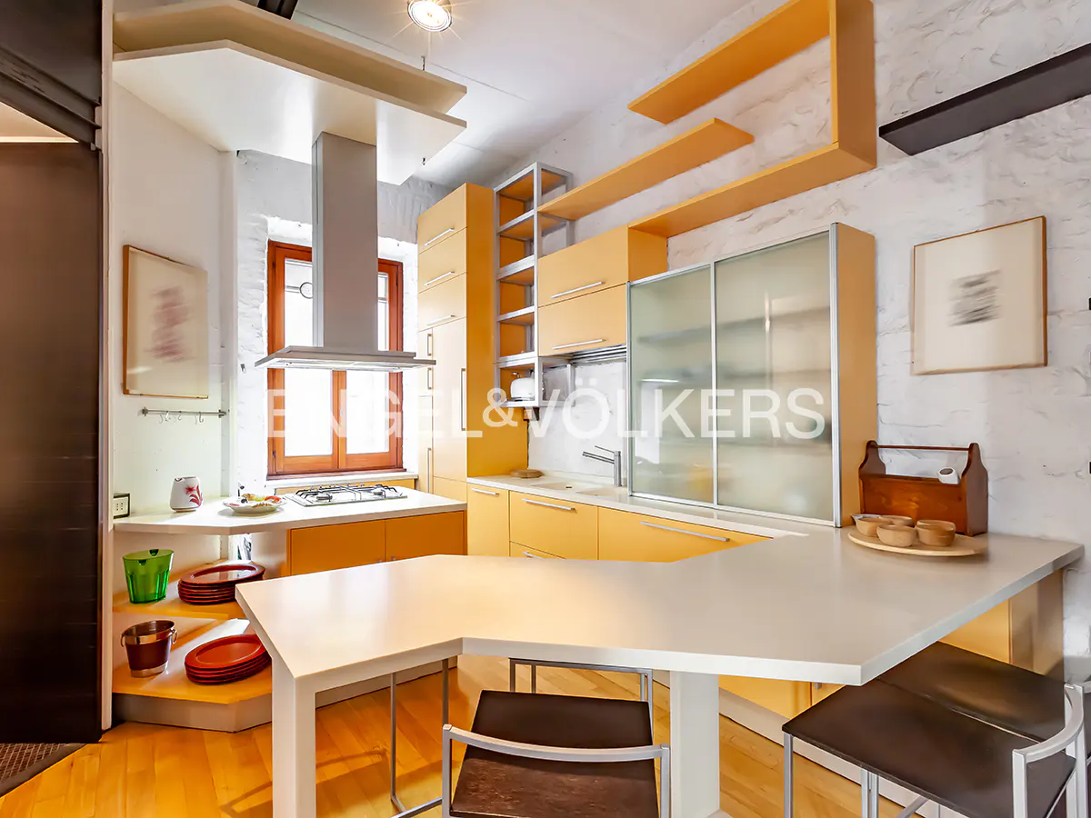 A modern kitchen with yellow cabinets, a white countertop island with chairs, and wooden floors.