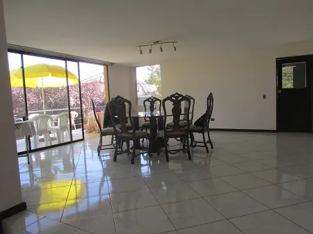 A bright, empty dining room with tile floors, a dark wood table and chairs, and a patio with a yellow umbrella.