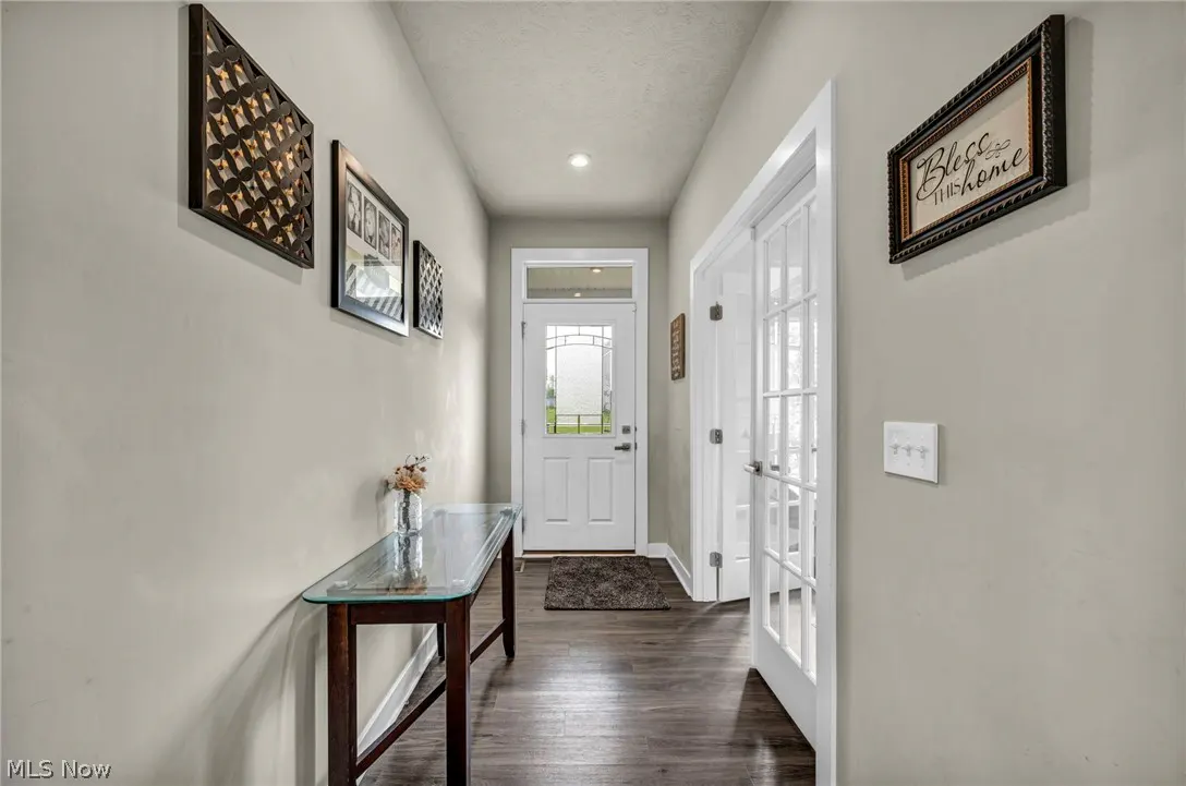 Hallway with gray walls, dark wood floors, and a white front door. A glass-topped table sits against the wall with framed art above.