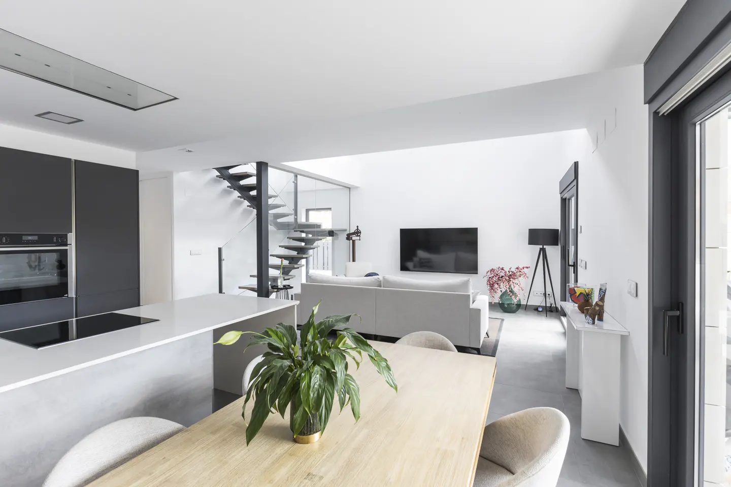 Open-concept living space with a kitchen island, dining table, and living room. A modern staircase leads to the upper level.