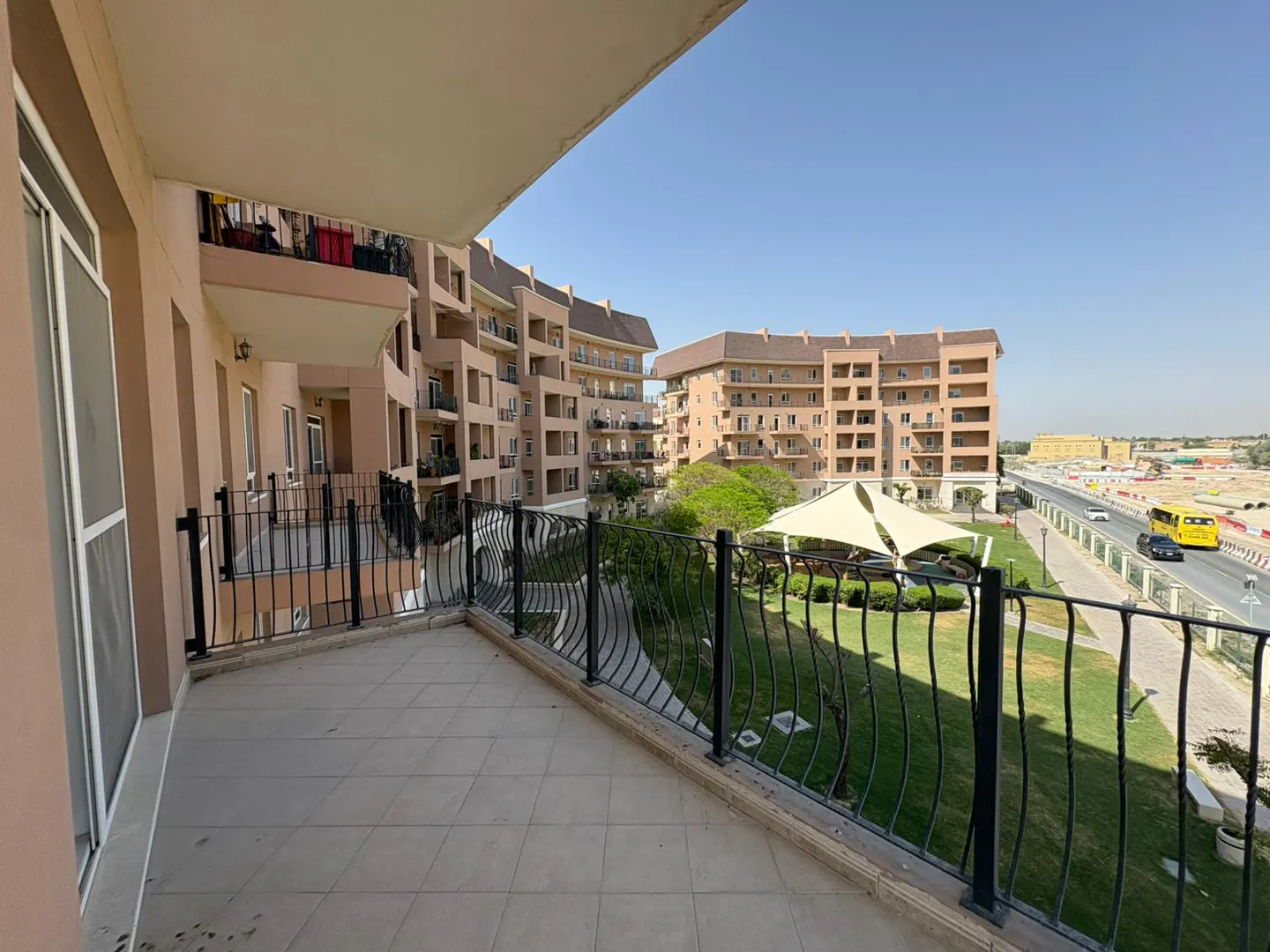 View from a balcony with black railings overlooking a green lawn, buildings, and a road with a yellow bus.