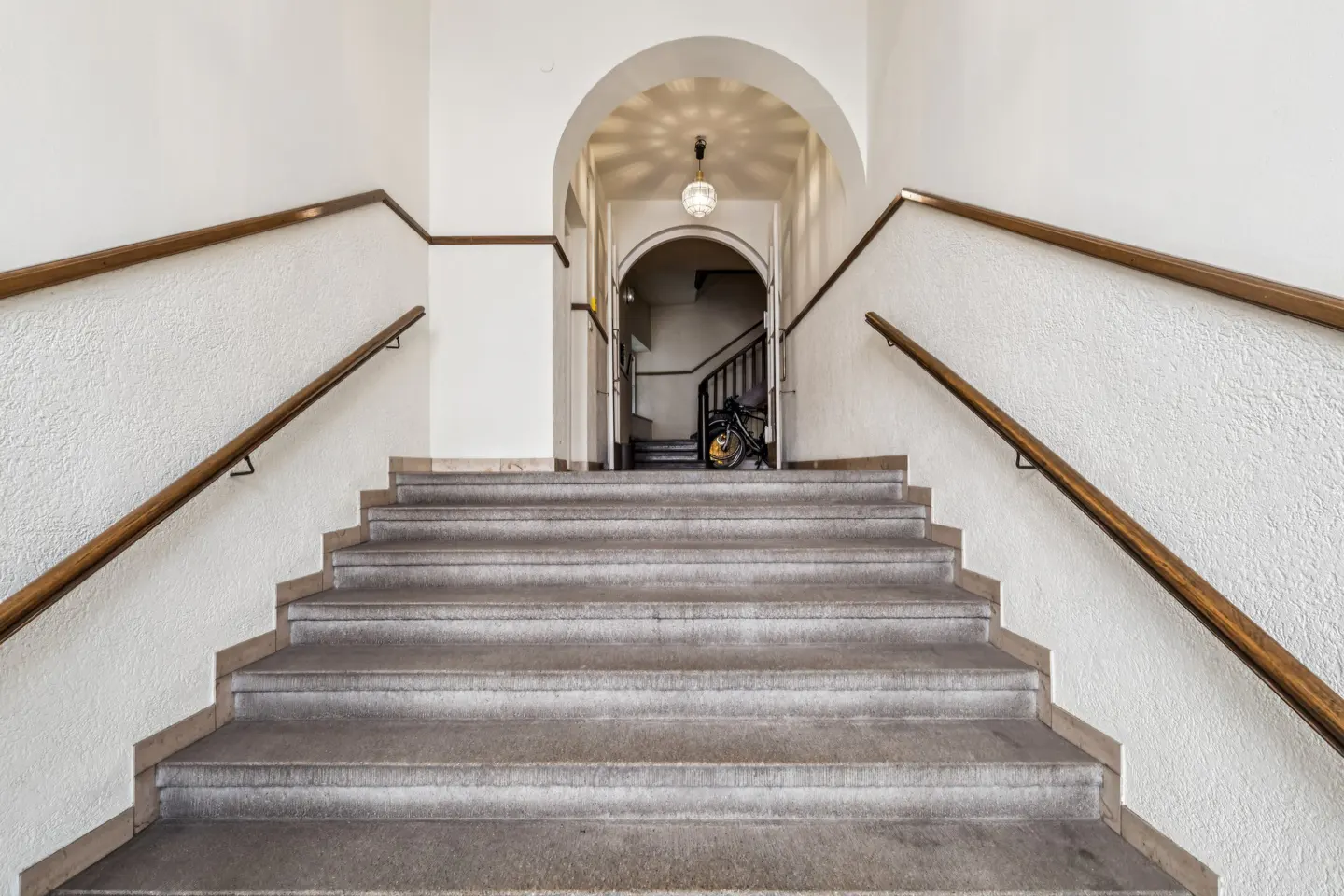 A staircase with wooden handrails leads to an arched doorway with a bicycle parked inside.