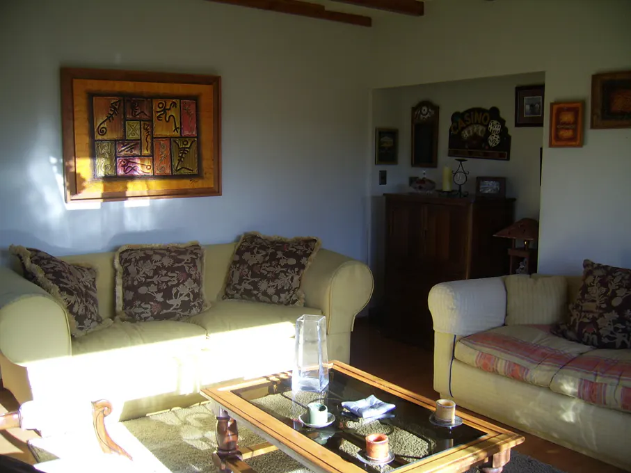 Living room with a yellow sofa, patterned pillows, and a glass-topped coffee table. Artwork hangs on the light gray walls.