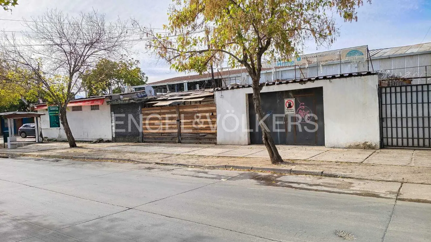 Street view of a white wall with wooden and metal gates, trees, and the Engel & Völkers logo.