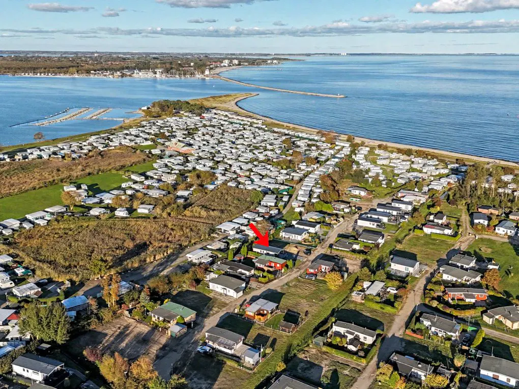 Aerial view of a coastal community with small houses, a beach, and a blue sea under a partly cloudy sky. An arrow points to a specific house.