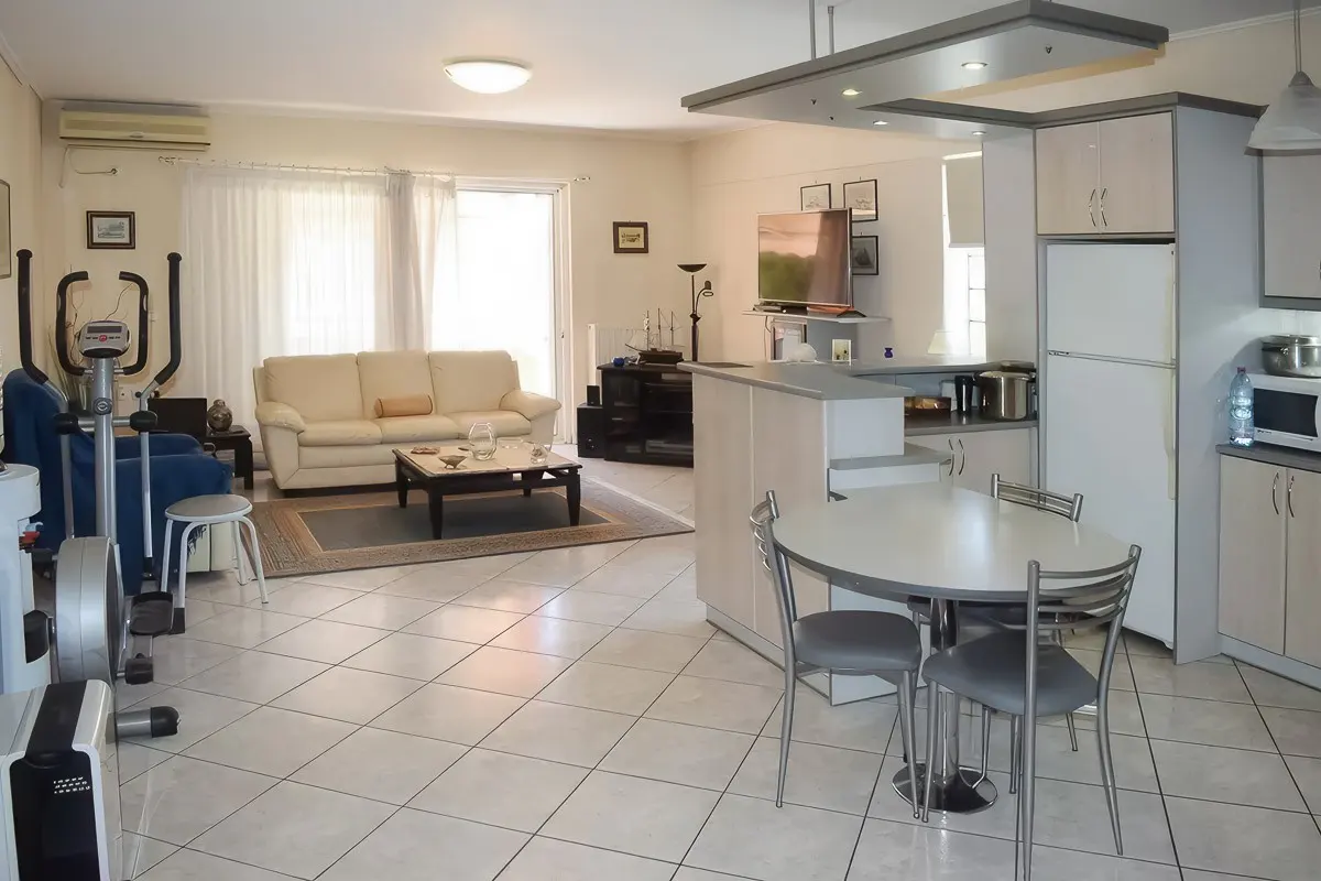 Open-concept living space with white tile floors, a cream sofa, and a kitchen with a round table and gray chairs.