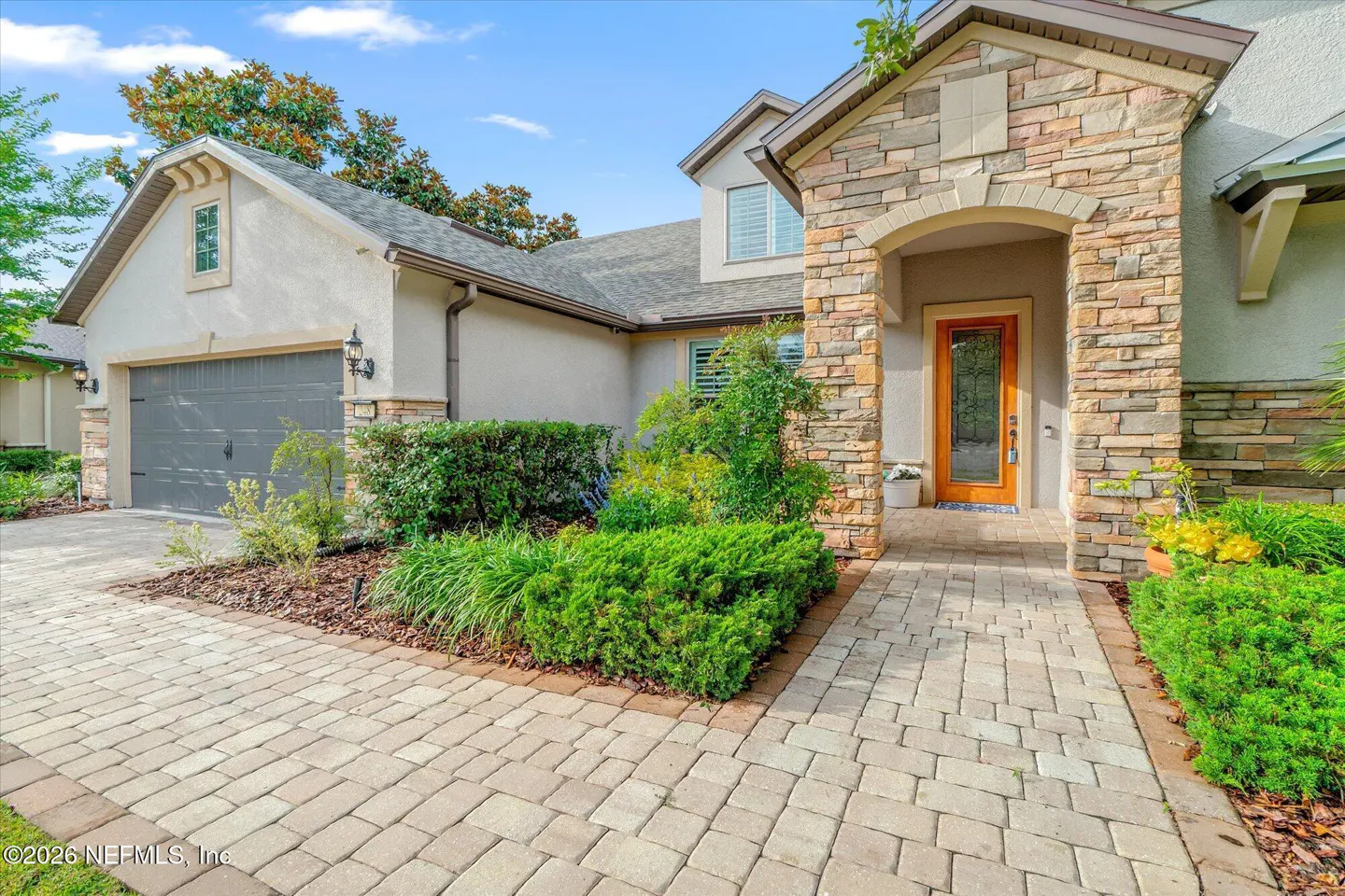 Exterior of a suburban home with a stone facade, gray garage, and a paved walkway leading to a wooden front door.