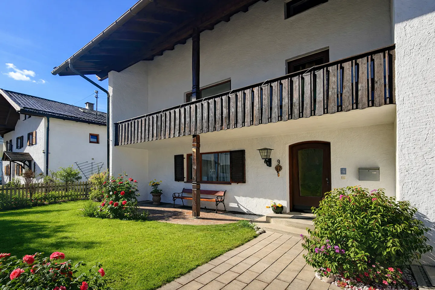Exterior of a white two-story house with a wooden balcony and a green lawn.