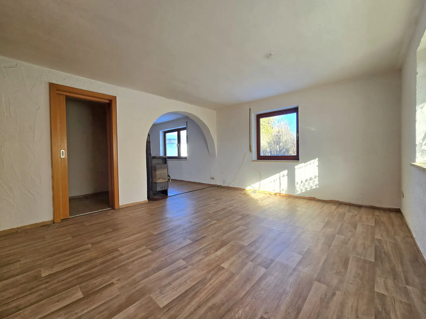 Empty room with wood-look flooring, white walls, and natural light. A doorway and arched opening lead to other rooms.