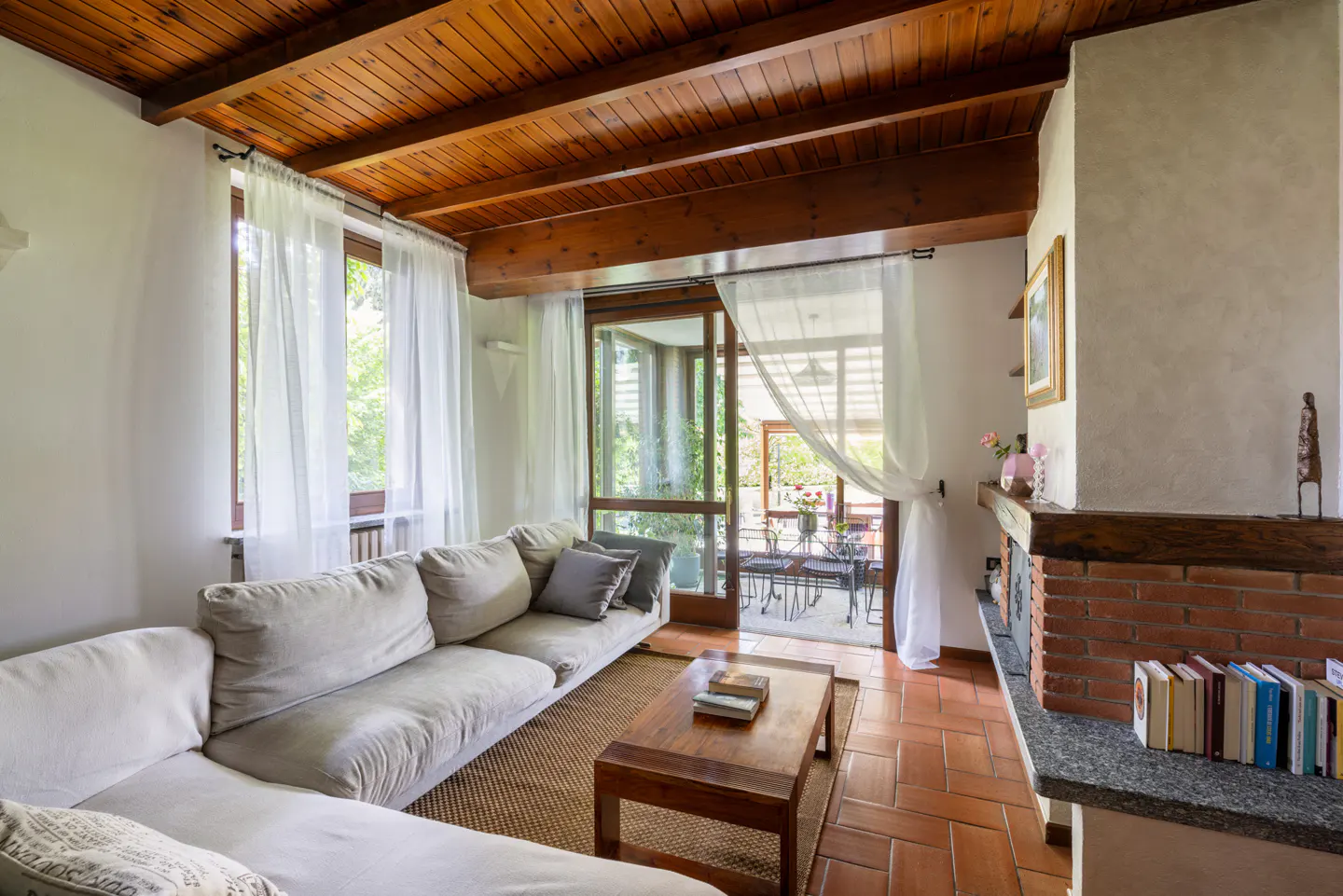 Living room with a beige sectional sofa, wooden ceiling, brick fireplace, and patio doors leading to an outdoor seating area.