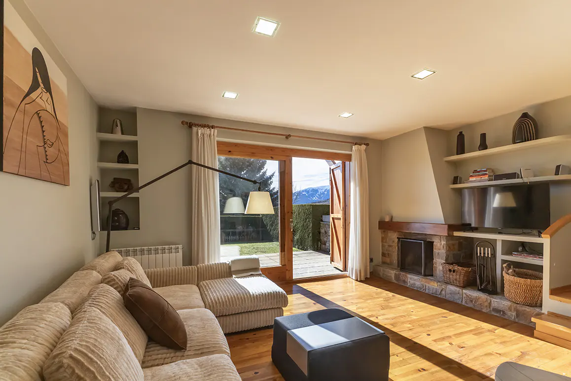 Living room with a beige sectional sofa, stone fireplace, and open doors to a patio with mountain views. Hardwood floors and recessed lighting.