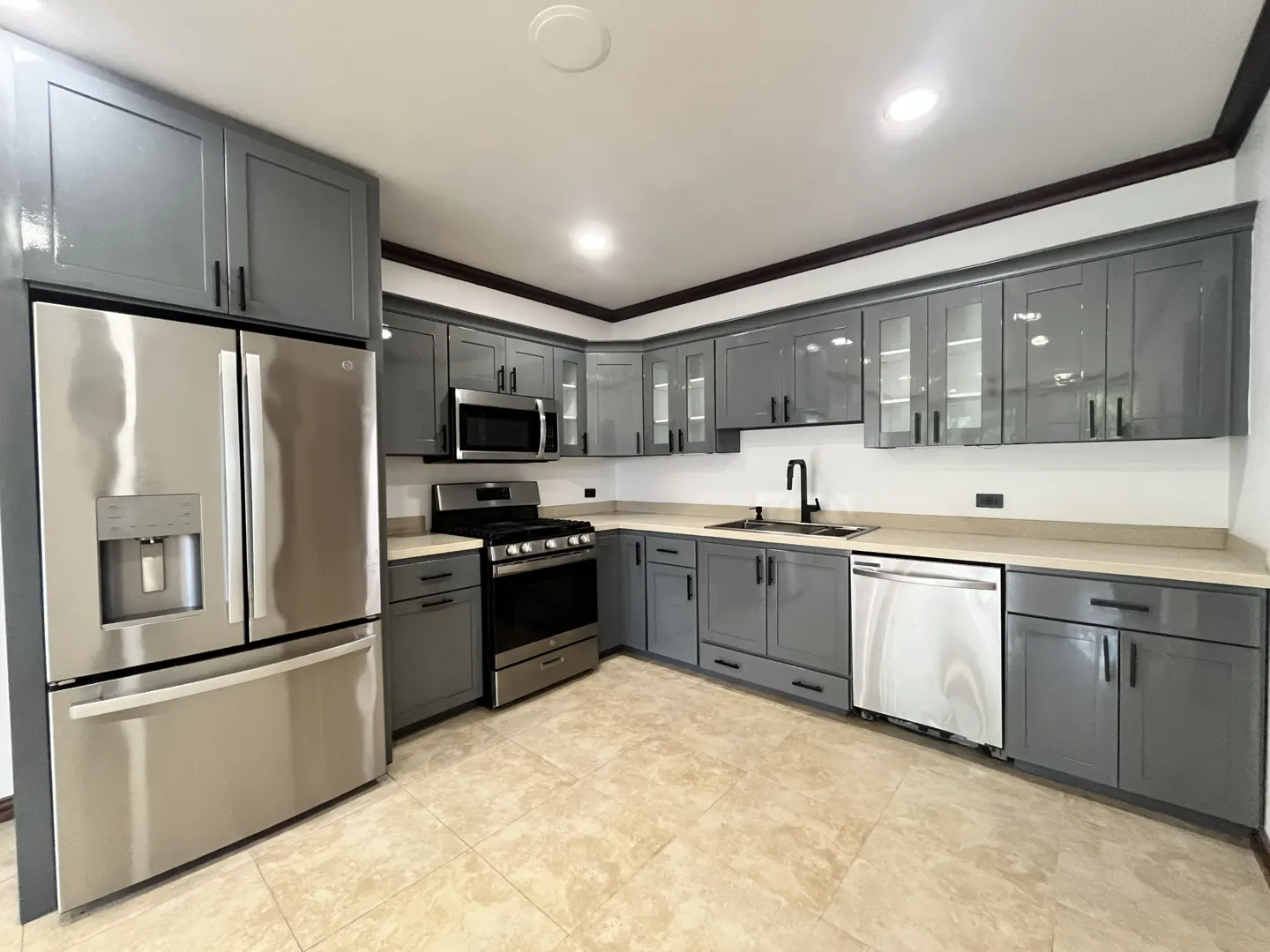A modern kitchen with gray cabinets, stainless steel appliances, and light beige countertops. The floor is tiled in a light beige color.