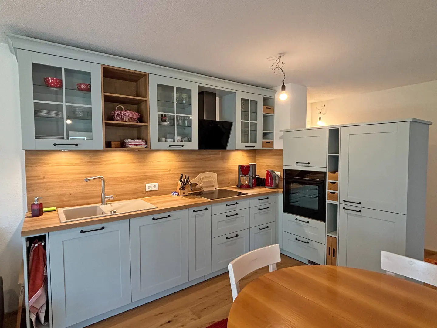 A bright kitchen with light blue cabinets, wood countertops, and a round wooden table in the foreground.
