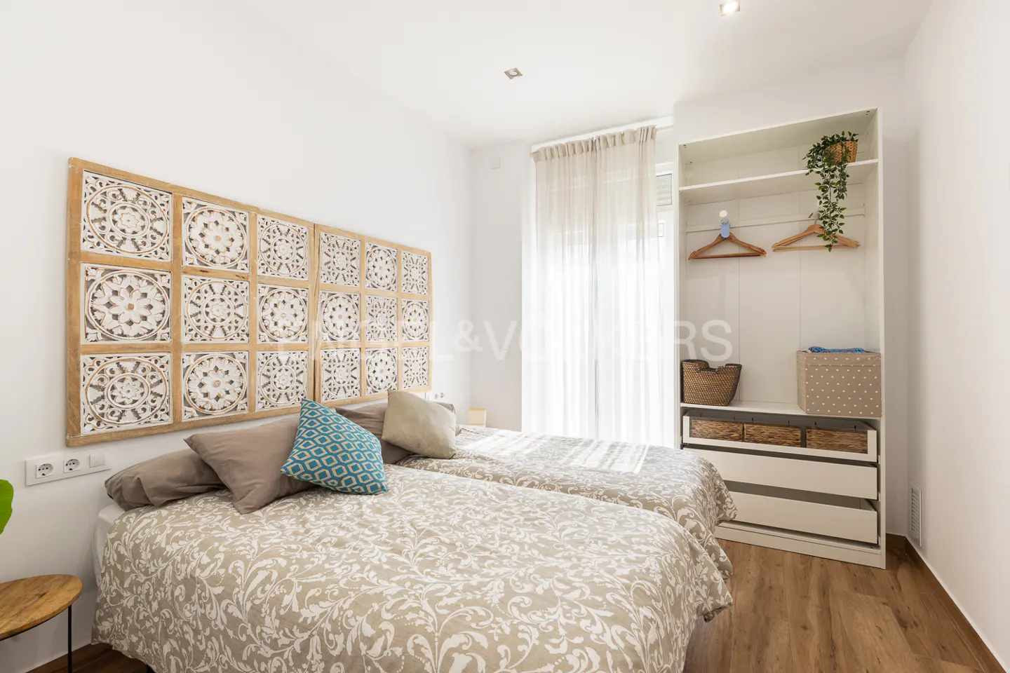 Bedroom with two twin beds, patterned headboard, white walls, and open white closet with shelves and drawers.