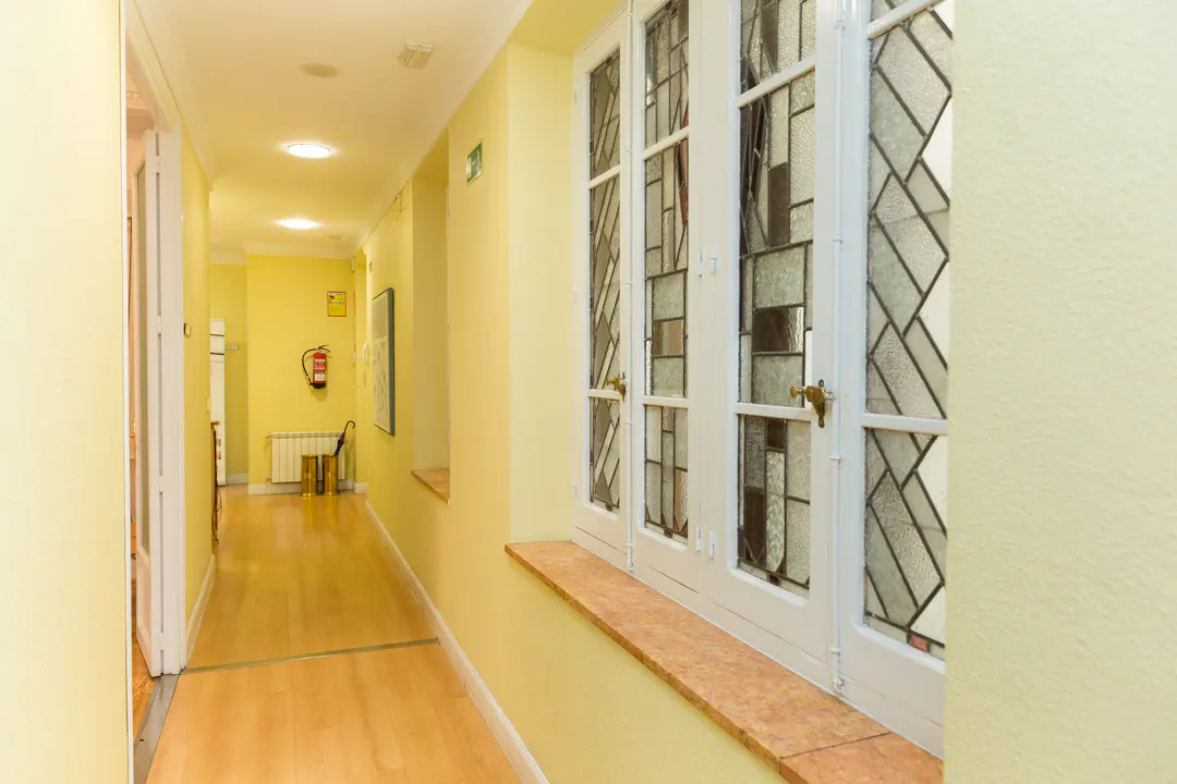 Hallway with yellow walls and wood floors. A white window with decorative glass is on the right. A fire extinguisher is visible down the hall.
