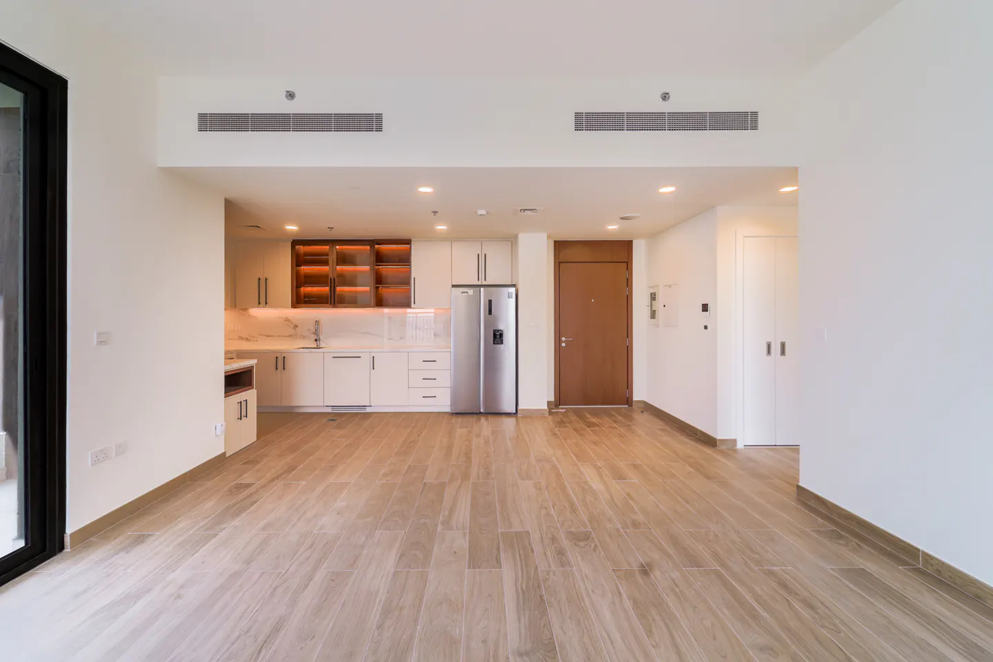 Bright, modern apartment interior with wood-look tile flooring, white walls, and a kitchen with stainless steel appliances.