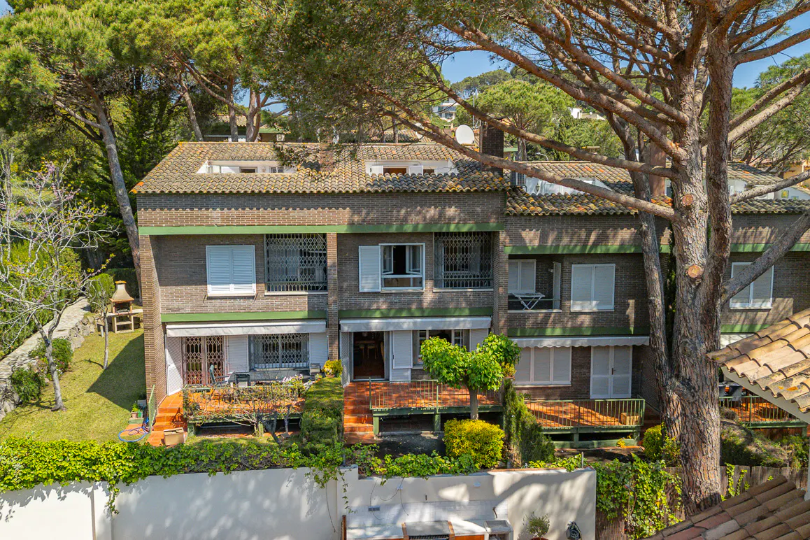 Two-story brick townhouse with a red tile roof, surrounded by green trees and landscaping.