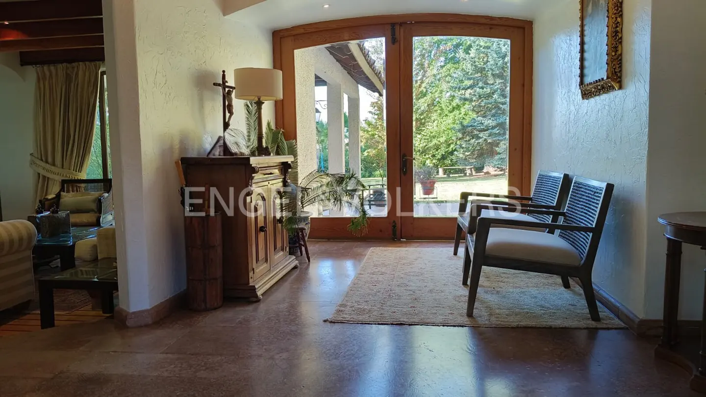 A home's entryway features wooden double doors, two chairs, and a wooden cabinet with a lamp.