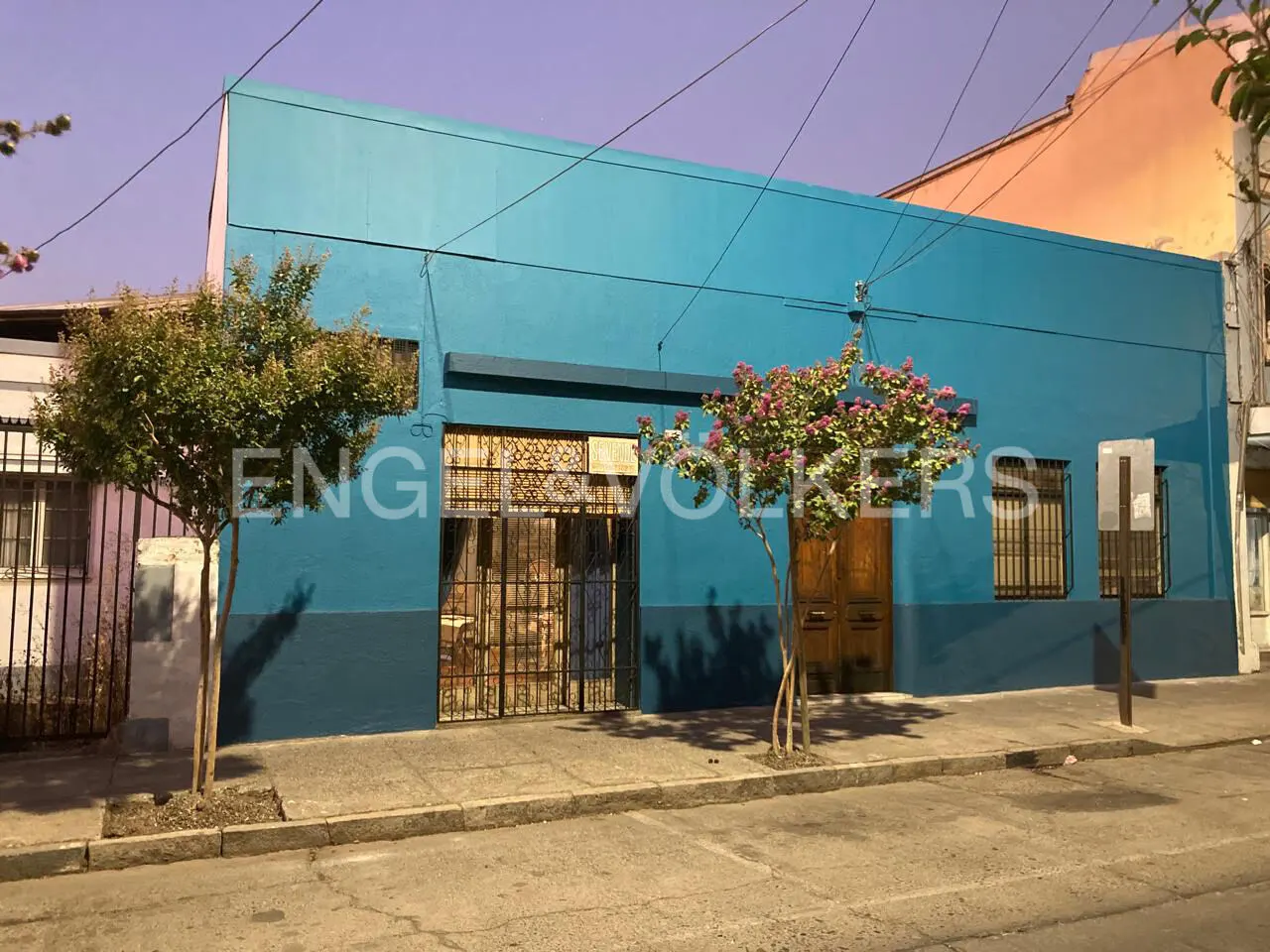 A two-story blue building with a barred window and door, and two small trees in front.